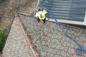 PorterVac technician in a safety harness vacuuming debris from the gutters of a Melbourne tile roof