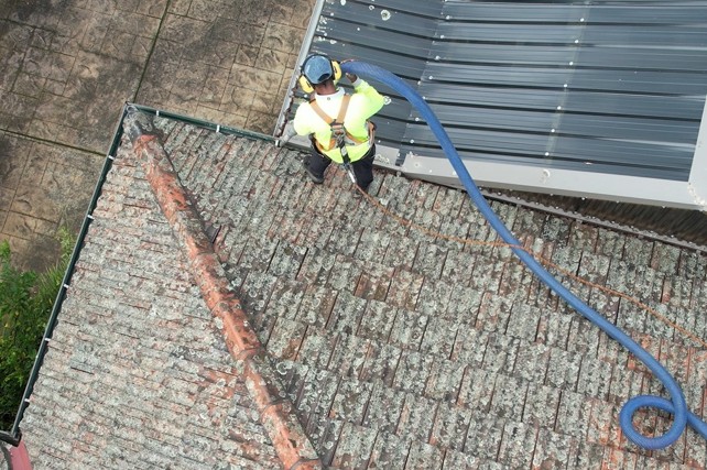 PorterVac technician in a safety harness vacuuming debris from the gutters of a Melbourne tile roof