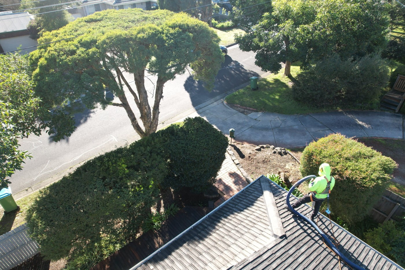 PorterVac technician feeding a vacuum hose along the gutter line of an old tile roof beside an evaporative cooler