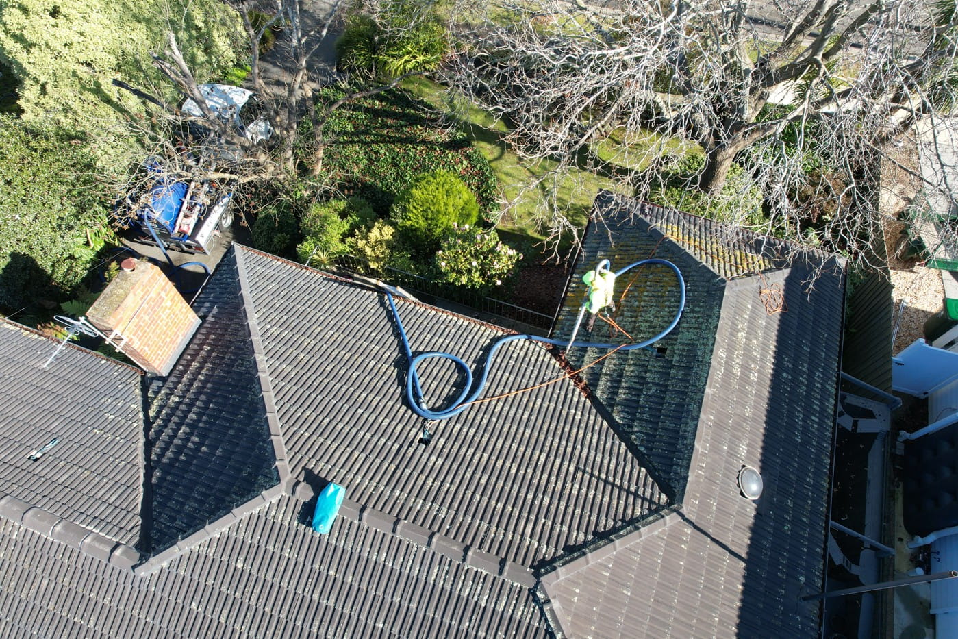 PorterVac technician on a tiled Forest Hill roof feeding a vacuum hose along the gutter line